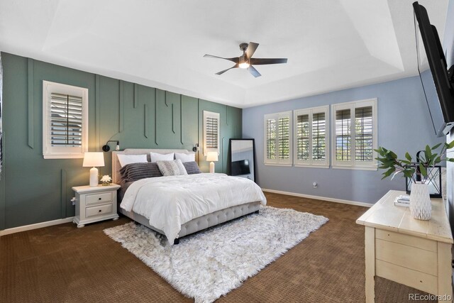 bedroom featuring a raised ceiling, baseboards, dark colored carpet, and ceiling fan