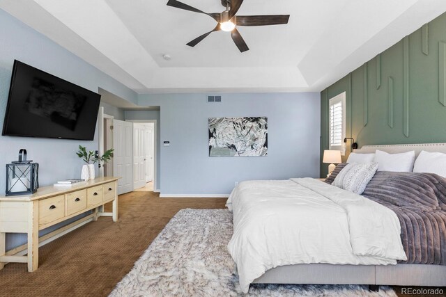 carpeted bedroom with baseboards, a tray ceiling, visible vents, and ceiling fan