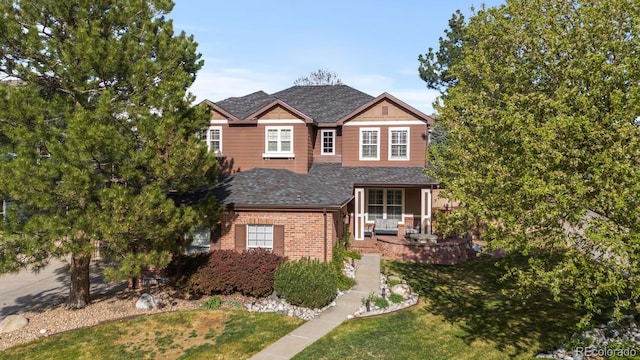 traditional-style home with roof with shingles, covered porch, a front lawn, and brick siding