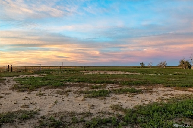 yard at dusk featuring a rural view and fence