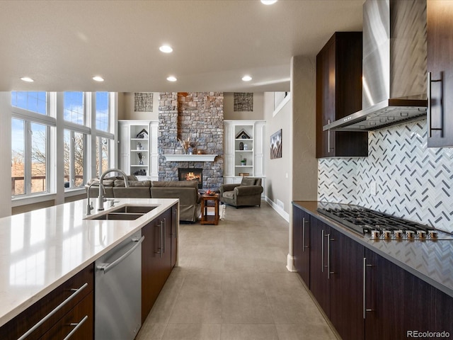 kitchen with appliances with stainless steel finishes, tasteful backsplash, wall chimney exhaust hood, sink, and a stone fireplace