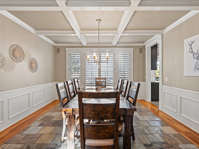 dining space with a wainscoted wall, dark wood-style floors, beam ceiling, and an inviting chandelier