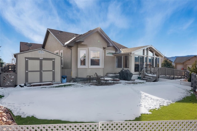 snow covered back of property with a deck, a storage shed, and a sunroom