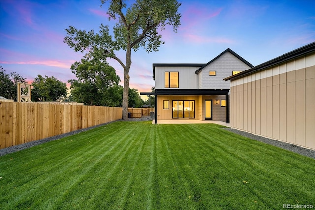 back house at dusk featuring a yard and a patio