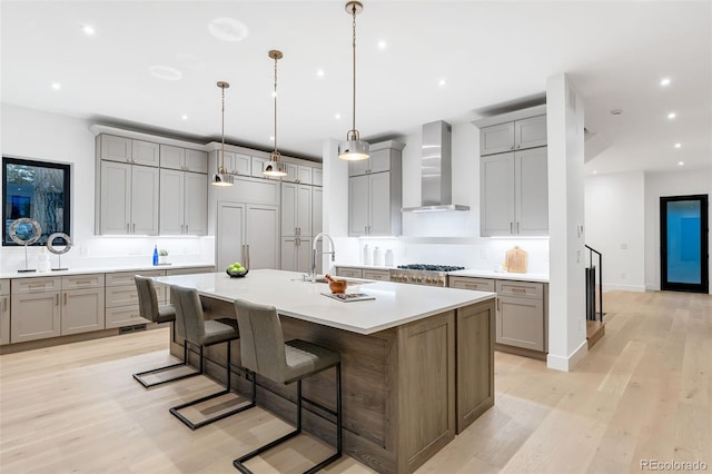 kitchen featuring light hardwood / wood-style flooring, a large island with sink, wall chimney range hood, a breakfast bar area, and pendant lighting