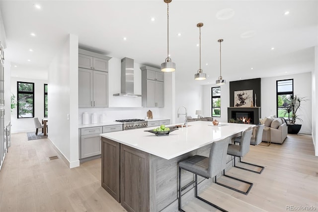 kitchen with a kitchen breakfast bar, decorative light fixtures, wall chimney exhaust hood, light hardwood / wood-style flooring, and a large island with sink