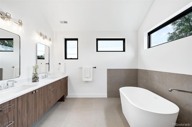 bathroom with lofted ceiling, a healthy amount of sunlight, a washtub, and vanity