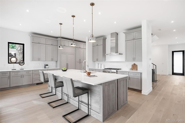 kitchen with pendant lighting, a kitchen bar, an island with sink, wall chimney exhaust hood, and light hardwood / wood-style floors