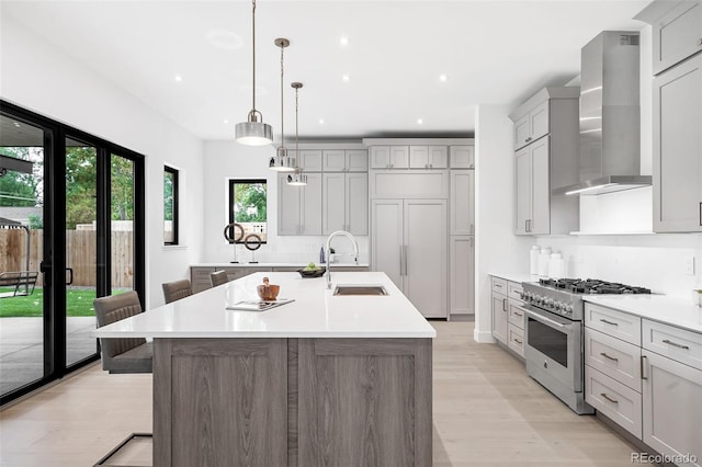 kitchen with wall chimney exhaust hood, a spacious island, pendant lighting, stainless steel stove, and sink