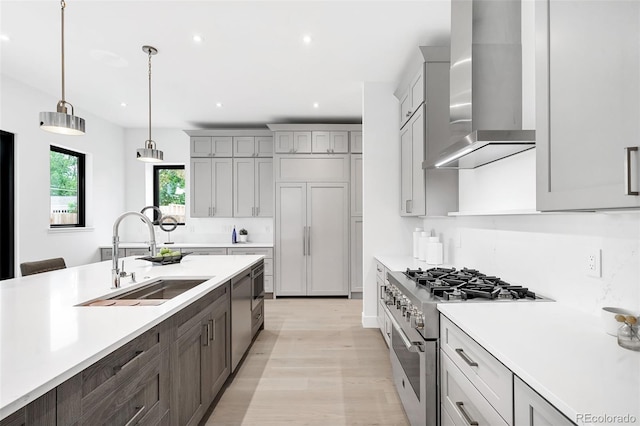 kitchen with pendant lighting, light hardwood / wood-style flooring, stainless steel appliances, sink, and wall chimney range hood