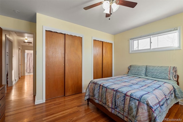 bedroom with two closets, light hardwood / wood-style flooring, and ceiling fan