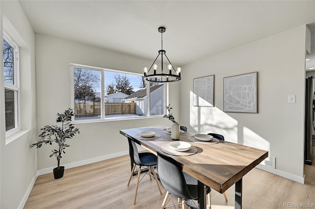 dining space with light hardwood / wood-style floors, plenty of natural light, and an inviting chandelier