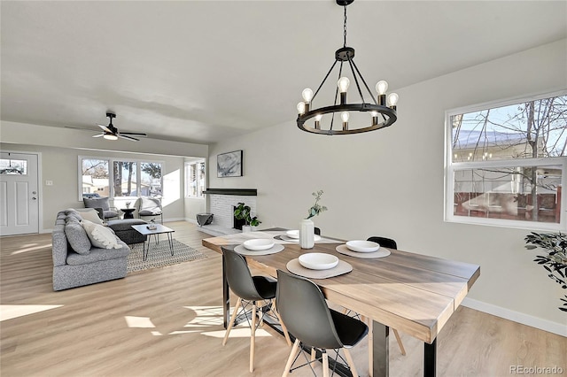 dining room with ceiling fan with notable chandelier, a brick fireplace, and light hardwood / wood-style flooring