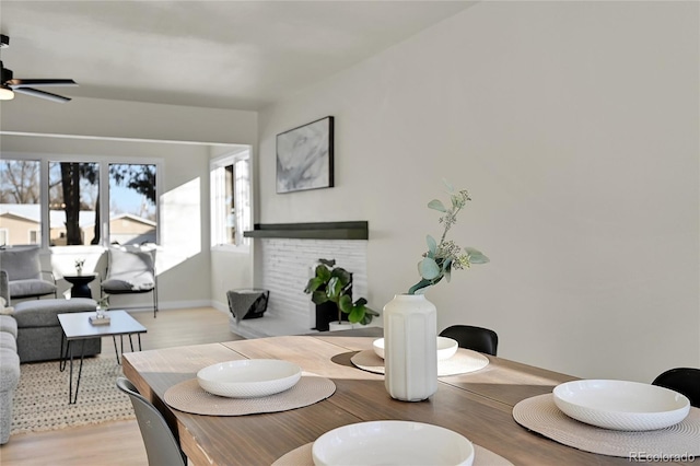 dining room with a fireplace, light hardwood / wood-style flooring, and ceiling fan