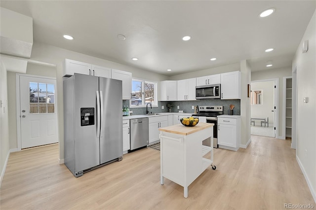 kitchen with appliances with stainless steel finishes, sink, a kitchen island, white cabinets, and light wood-type flooring