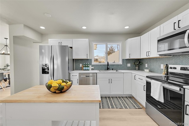 kitchen with hanging light fixtures, appliances with stainless steel finishes, sink, white cabinets, and wood counters