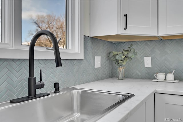 room details featuring light stone counters, sink, white cabinetry, and backsplash