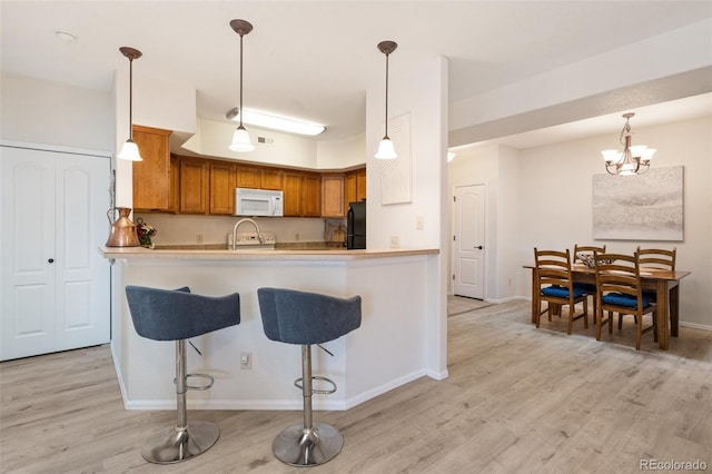 1816 Montura Vw Unit 204, Colorado Springs, CO 80919 - kitchen featuring baseboards, white microwave, light wood-style floors, a breakfast bar area, and brown cabinetry