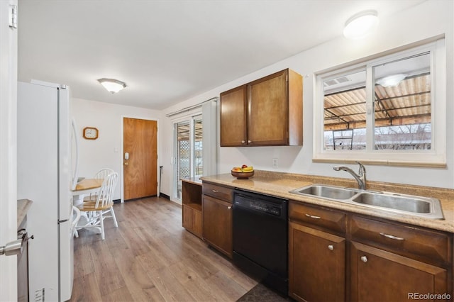 kitchen with light wood finished floors, light countertops, black dishwasher, freestanding refrigerator, and a sink