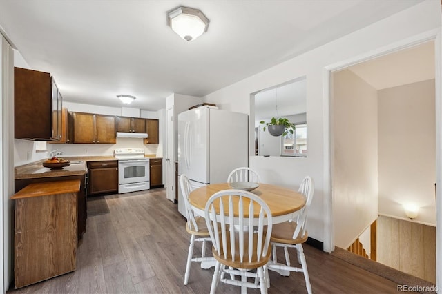 kitchen with under cabinet range hood, white appliances, dark wood-style flooring, and a sink