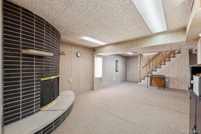 finished basement with stairway, carpet floors, wooden walls, and a fireplace