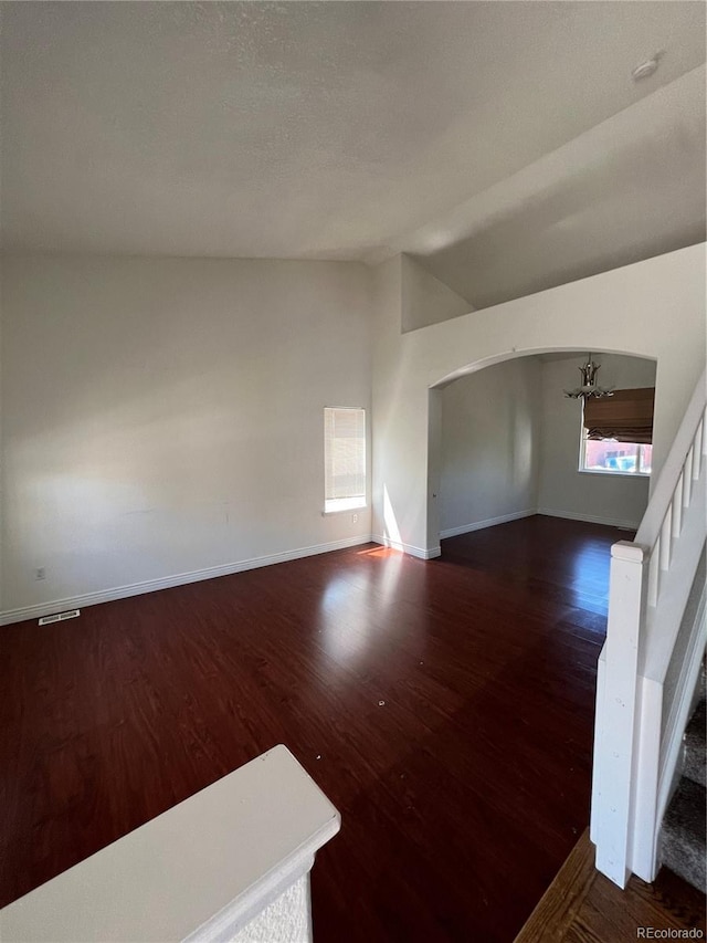 unfurnished living room featuring dark wood-type flooring, vaulted ceiling, and an inviting chandelier