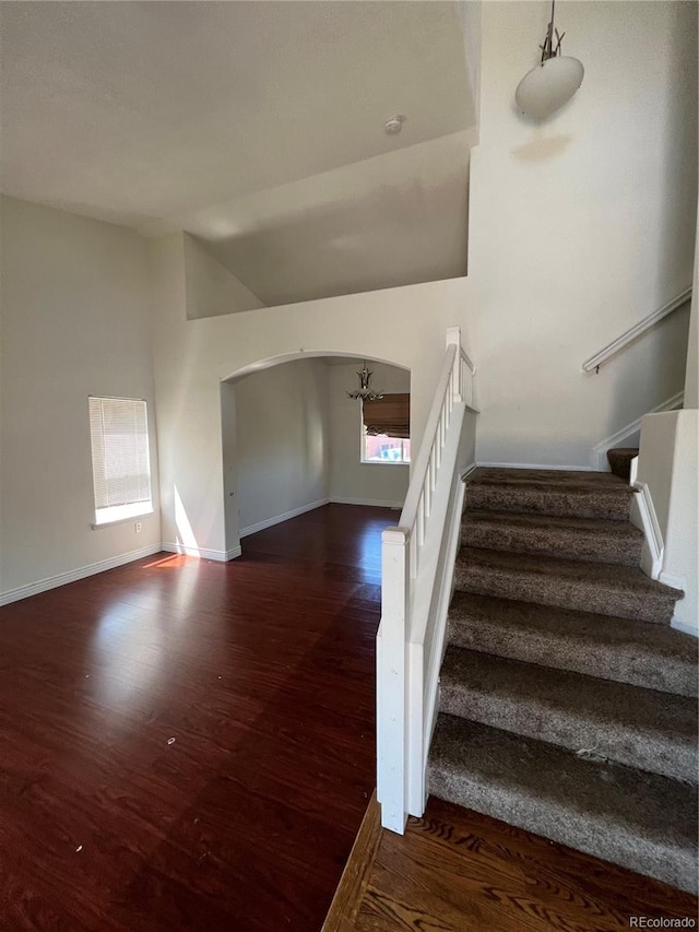 stairs featuring vaulted ceiling, wood-type flooring, a wealth of natural light, and a chandelier