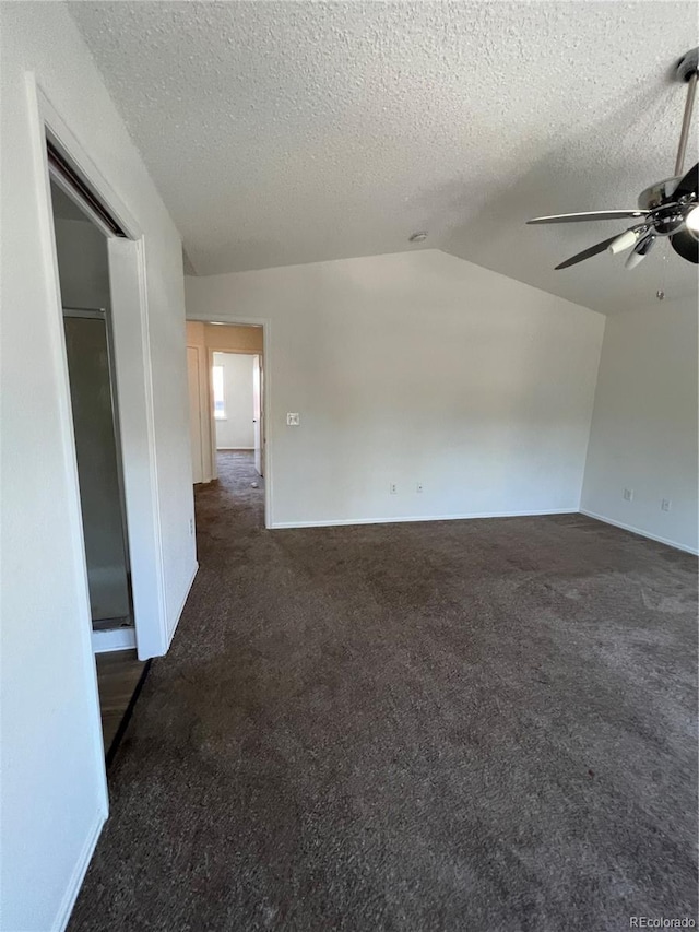 spare room featuring dark carpet, vaulted ceiling, a textured ceiling, and ceiling fan