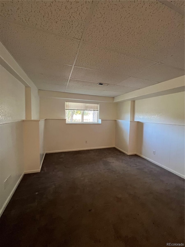 unfurnished room featuring a drop ceiling and dark colored carpet