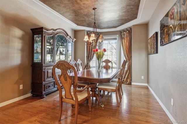 dining space with a tray ceiling, a chandelier, and wood-type flooring