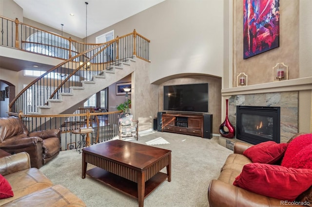 carpeted living room with a high end fireplace and a towering ceiling