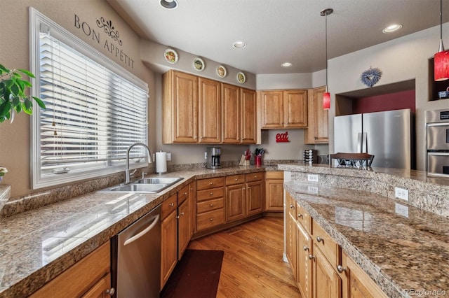 kitchen with appliances with stainless steel finishes, light wood-type flooring, decorative light fixtures, and sink