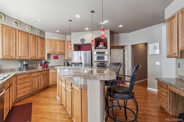 kitchen with light stone counters, stainless steel appliances, light hardwood / wood-style flooring, a center island, and a breakfast bar area