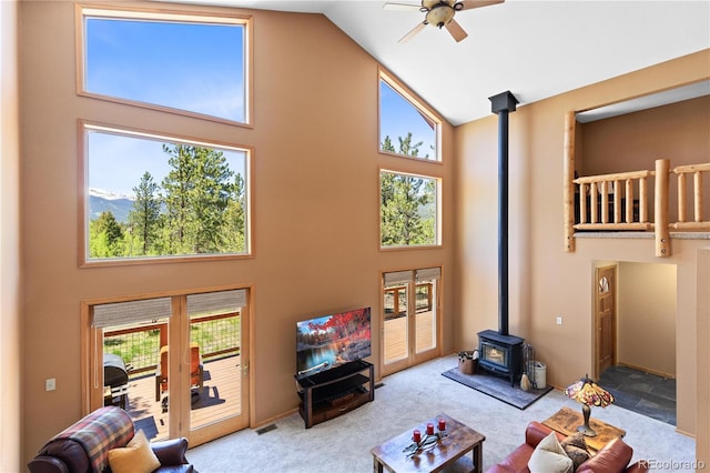 carpeted living room featuring visible vents, high vaulted ceiling, ceiling fan, and a wood stove