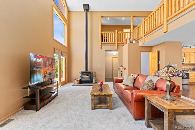 carpeted living area featuring a wood stove, visible vents, a towering ceiling, and baseboards