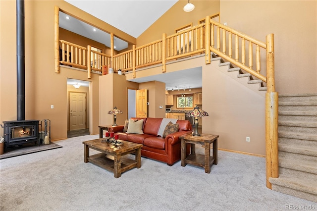 carpeted living area featuring baseboards, stairway, a wood stove, high vaulted ceiling, and track lighting