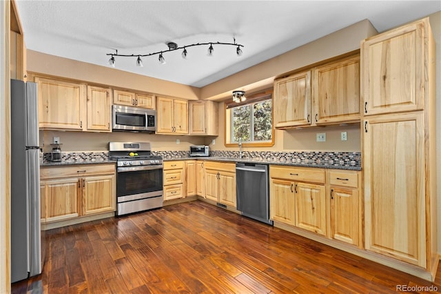 kitchen featuring appliances with stainless steel finishes, dark countertops, dark wood finished floors, and light brown cabinetry