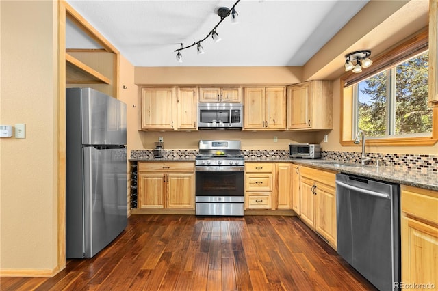 kitchen featuring light stone counters, dark wood finished floors, stainless steel appliances, light brown cabinetry, and a sink