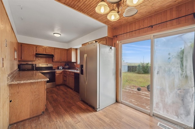 6545 Brook Forest Dr, Colorado Springs, CO 80911 - kitchen featuring appliances with stainless steel finishes, under cabinet range hood, dark wood finished floors, wooden walls, and brown cabinetry