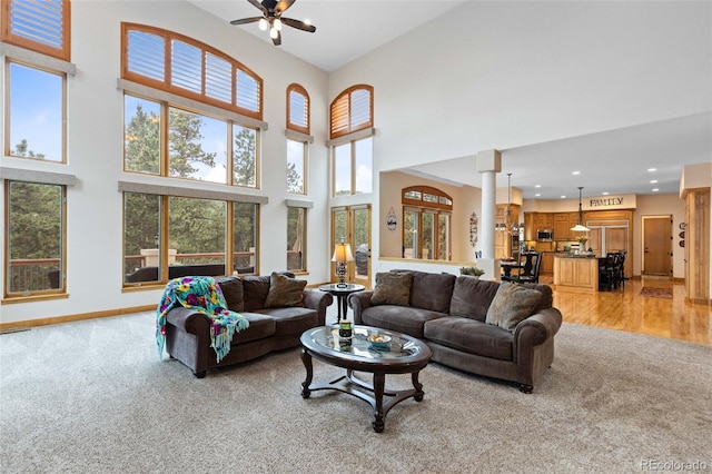 living room featuring light carpet, ceiling fan, decorative columns, and a towering ceiling