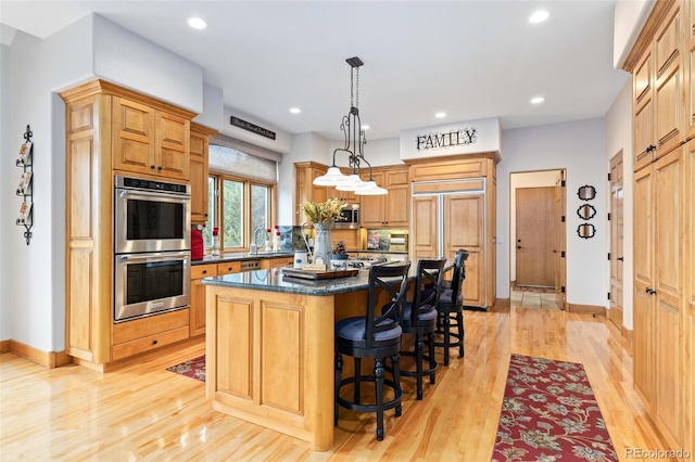 kitchen with stainless steel appliances, hanging light fixtures, light hardwood / wood-style flooring, a kitchen island, and sink