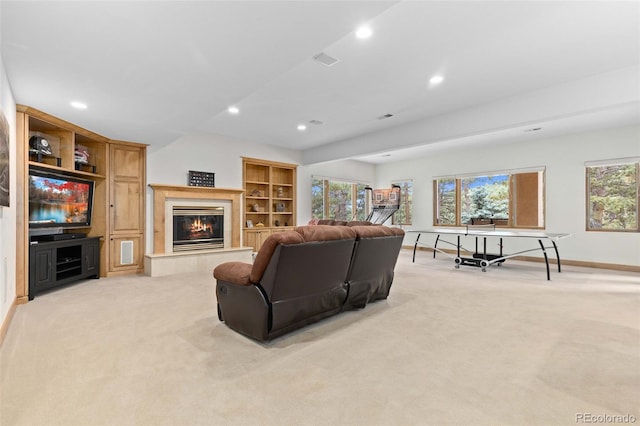 living room featuring built in features, a tile fireplace, light carpet, and a healthy amount of sunlight