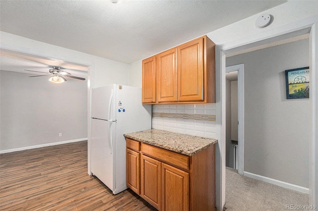2308 Lima St, Aurora, CO 80010 - kitchen featuring freestanding refrigerator, decorative backsplash, ceiling fan, light stone counters, and wood finished floors