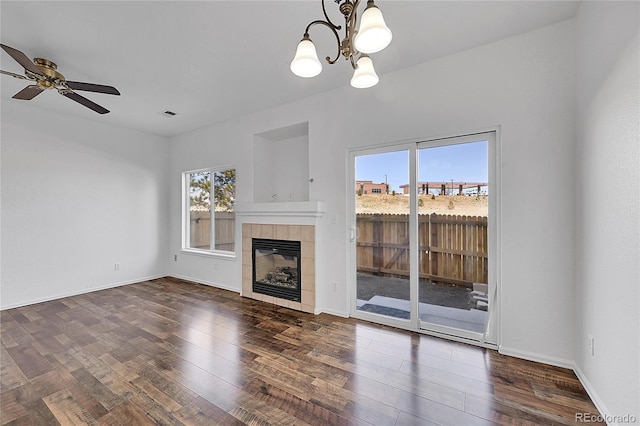 unfurnished living room featuring baseboards, dark wood finished floors, a tiled fireplace, and ceiling fan with notable chandelier