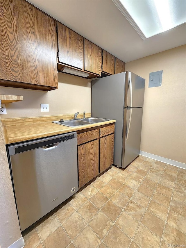 kitchen featuring light countertops, stone finish floor, brown cabinetry, appliances with stainless steel finishes, and a sink