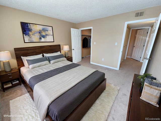 bedroom with a textured ceiling, a spacious closet, visible vents, light carpet, and baseboards