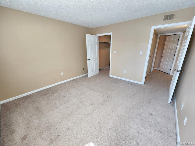 unfurnished bedroom featuring a textured ceiling, light colored carpet, baseboards, and visible vents