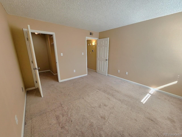 unfurnished bedroom featuring baseboards, a textured ceiling, a walk in closet, visible vents, and carpet