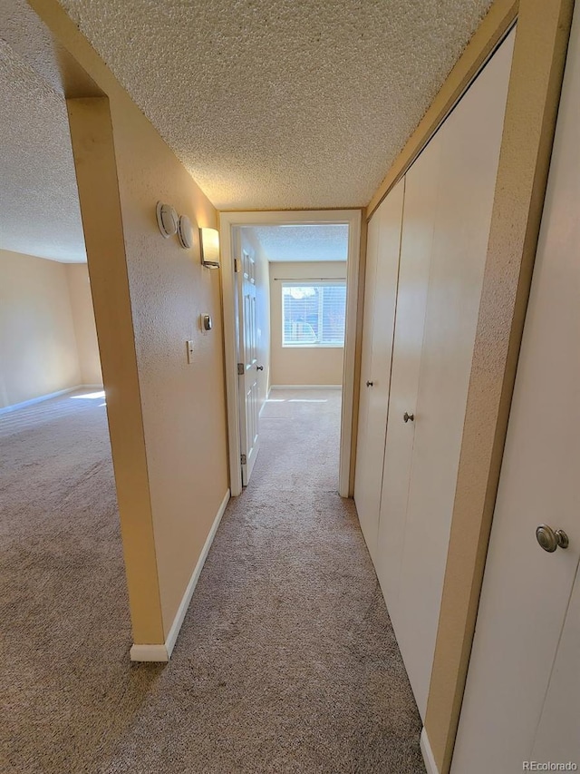 corridor with light carpet, a textured ceiling, and baseboards