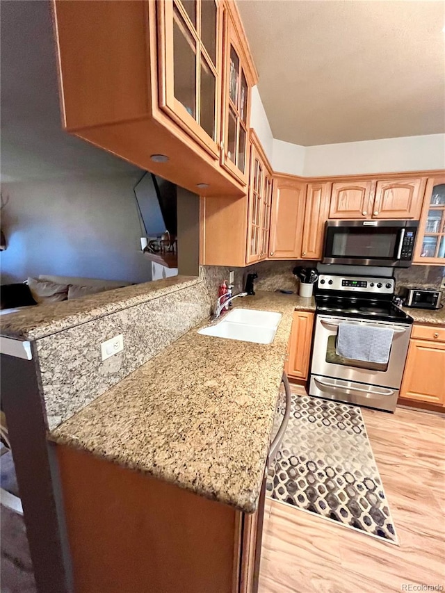 kitchen featuring kitchen peninsula, sink, light stone countertops, appliances with stainless steel finishes, and light hardwood / wood-style floors